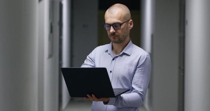 Serious engineer in formal attire opens laptop standing in hallway. Focused businessman opens modern computer preparing to work on complex business document