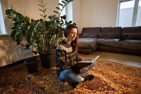 Woman in cozy sweater reading a book while sitting on a patterned rug