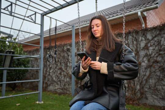 Woman on swing using smartphone in backyard during overcast day