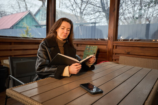 Woman reading a book on a wooden table in a cozy veranda during winter