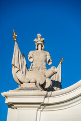 Obraz premium Stone sculpture of armored medieval figure with cannons and flags on ceremonial gate at Bratislava Castle. Historic architectural detail against deep blue sky in Slovakia