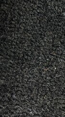 Fototapeta premium Vertical close-up texture of dark black rough woven carpet fabric background.