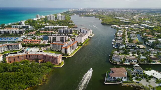 Aerial view of the Intracoastal Waterway featuring luxury residential buildings, lush greenery, and a boat cruising through the channel in Boca Raton, Florida, United States.