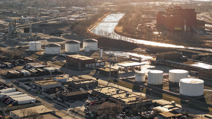 Fototapeta premium Industrial zone with storage tanks and river at sunset in American mid west rust belt.