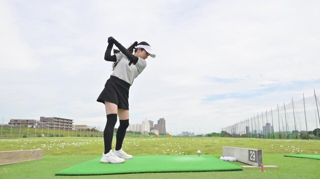 [スローモーション]打ちっぱなしのゴルフ練習場でドライバーショットをスウィングする若い女性のゴルファーのスポーツイメージの動画　全身広角