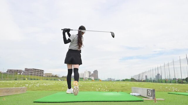 打ちっぱなしのゴルフ練習場でドライバーショットをスウィングする若い女性のゴルファーのスポーツイメージの動画　全身広角