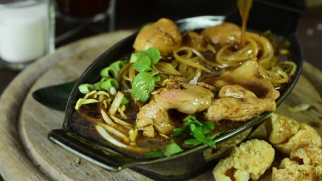 Pouring rich soup onto sizzling Thai boat noodles on a hot plate. Delicious street food with sliced pork, meatballs, and sprouts. Asian cuisine concept for mouth-watering food video.