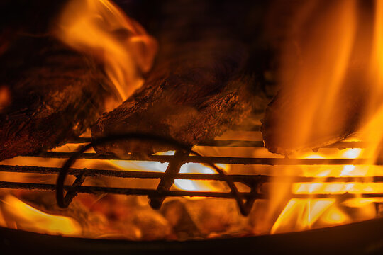 Flames dance around grilled meat at a summer barbecue in the backyard on a warm evening