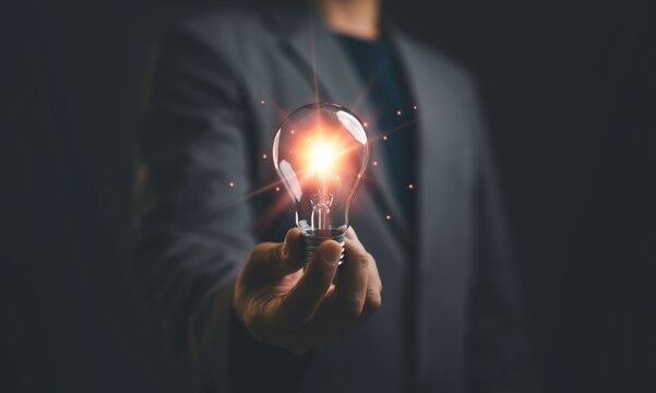Businessman holding glowing light bulb representing innovation, creative idea and business inspiration. Concept of startup success, leadership, technology and strategic thinking.