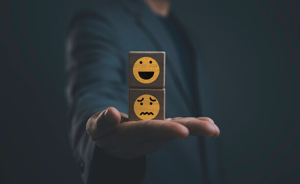 Positive and negative emotion concept with happy and unhappy face icons on wooden blocks in businessman hand. Symbol of emotional balance, mental health and customer satisfaction.