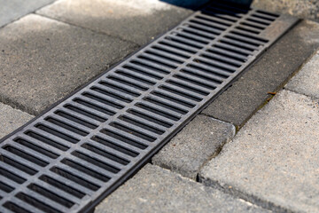 Fototapeta premium Metal grate over drainage channel in pavement, close-up. Urban stormwater management.