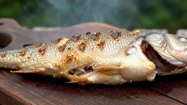 Freshly grilled sea bass resting on a rustic wooden cutting board with thin wisps of hot steam rising slowly into the air in a cinematic shot