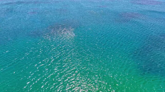 Aerial view of the sea surface with reflected sunlight. Mediterranean waves on a bright sunny day. Sea from a drone. Gentle ripples on the water's surface with light refraction. Sea wave close-up.