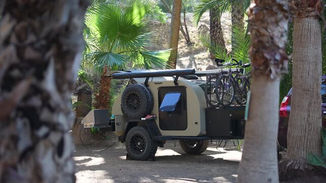Teardrop camper trailer is parked in a desert oasis surrounded by palm trees in San Ignacio Mexico during the morning light.