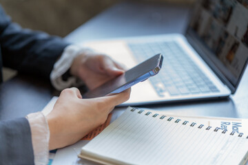 Fototapeta premium Close-up of a businesswoman using a smartphone with a laptop and notebook at an office desk.