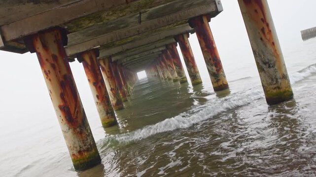 Rusty pier pillars immersed in sea water with clockwise tilt camera capturing dynamic coastal scene