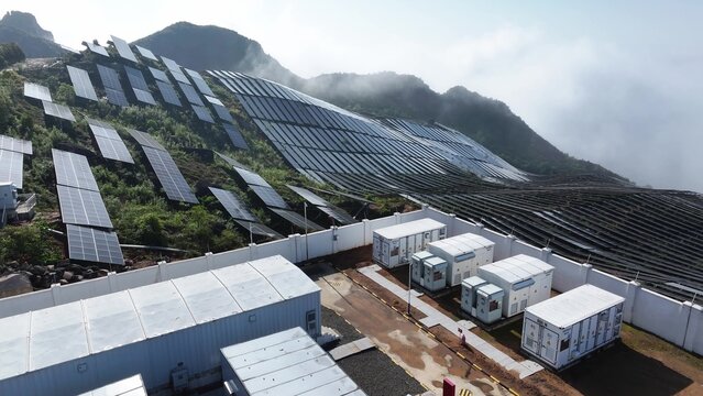 Solar power plant with photovoltaic panels and energy storage containers on a mountain slope