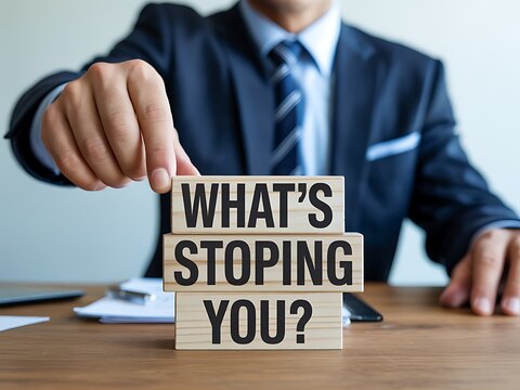 Professional male hand arranging wooden blocks displaying the phrase Whats Stoping You on a desk