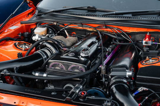 Engine bay of Toyota Supra A80 with 2JZ GTE engine. Tuned motor with black cylinder head and intake piping under the hood of an orange Toyota Supra mk4. Kyiv, Ukraine - May 16 2026