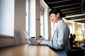 Fototapeta premium Asian businesswoman multitasking and working on laptop at modern office cafe creating concepts