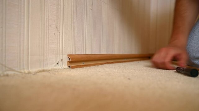 Man removing baseboard trim from carpeted interior room during renovation