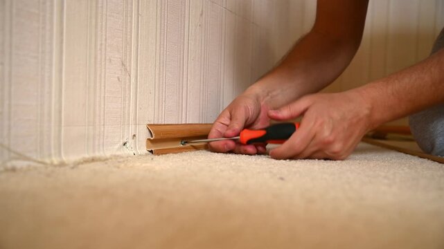 Man removing wooden baseboard molding along interior wall on carpet