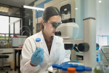 Fototapeta premium Female Scientist Looking Through Microscope While Holding Test Tube in Modern Research Laboratory
