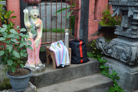 A high-angle view looking down from the front-left showcases a black gym sack, a silver water flask, and a white towel resting on stone pavilion steps in a lush park.