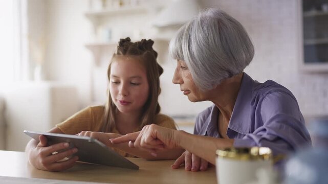 Smiling girl showing her granny a new educational game on smartphone, technology