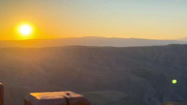 A panning video of mountains with beautifully overlapping layers of green and golden yellow at dawn in Xinjiang, China. The sun is rising with lens flares and warm tones.