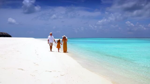 A beautiful family walks together on a tropical beach with turquoise ocean and white sand during their vacations in the Maldives islands