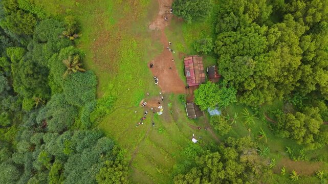 Aerial view of Bukit Pengilon with people walking near small buildings surrounded by lush green trees in Kecamatan Tepus, Daerah Istimewa Yogya, Indonesia.