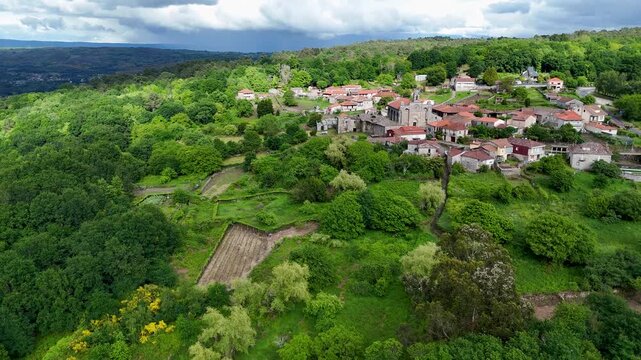 Aerial view of Iglesia de Santa Marina de Augas Santas surrounded by lush green forests and traditional stone houses in Augas Santas, Ourense, Spain.