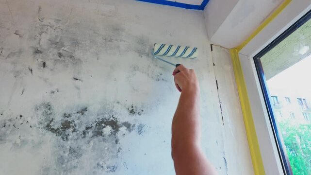 Person rolling primer over interior wall near window during renovation