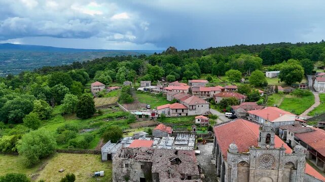 Aerial view of Iglesia de Santa Marina de Augas Santas, stone houses, and lush green forests in the village of Augas Santas, Ourense, Spain.