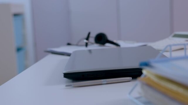 Focused professional typing on laptop keyboard at modern medical clinic office desk near pen document folder and smartphone with stethoscope background blur in quiet workspace