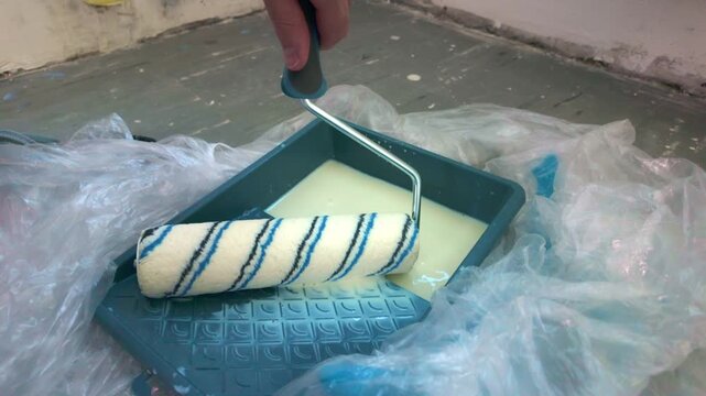 Roller being loaded and rolled in tray with primer on plastic covered floor