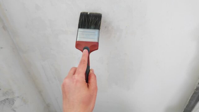 Hand brushing primer onto interior plaster wall in room corner