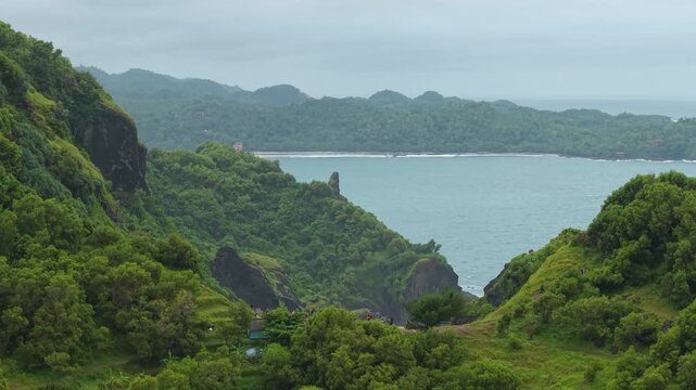 Aerial view of Bukit Pengilon with lush green hills overlooking the ocean under an overcast sky Kecamatan Tepus, Daerah Istimewa Yogya, Indonesia.