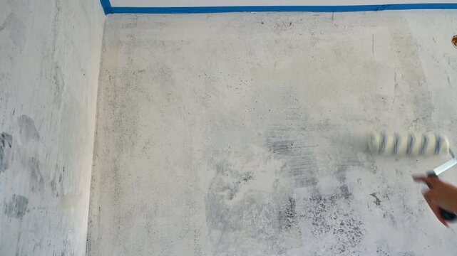 Person rolling primer over interior wall near ceiling edge