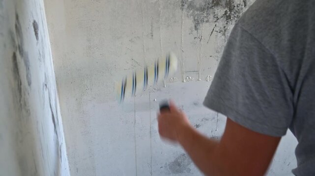 Man rolling paint roller across interior plaster wall during renovation