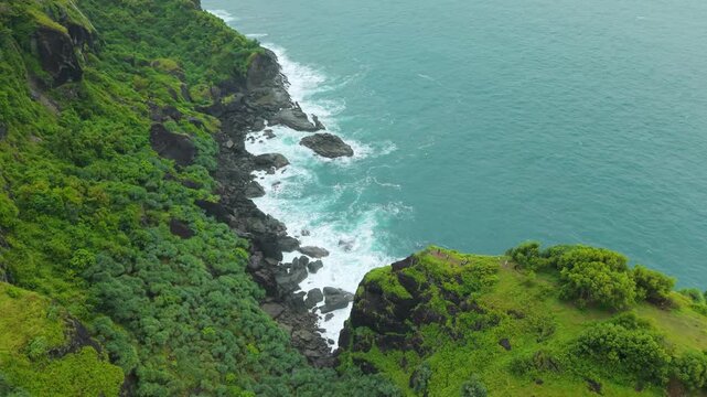 Aerial view of Bukit Pengilon cliffs with lush green vegetation and waves crashing on rocks in Kecamatan Tepus, Daerah Istimewa Yogya, Indonesia.