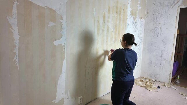 Woman scraping wallpaper off interior wall during home renovation  in timelapse