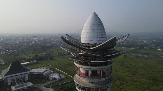 Aerial view of Menara Pandang Teratai with its lotus-shaped top and observation deck overlooking green fields in Kecamatan Purwokerto Timur, Jawa Tengah, Indonesia.