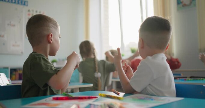 Young children seated at classroom desks with pencils and worksheets, listening during an interactive lesson in a bright early education room