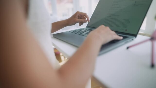 Overshoulder writer typing on laptop near sunny window