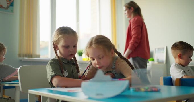 Young children drawing with colored pencils at classroom desks while a teacher supervises, capturing creative learning and quiet preschool activity
