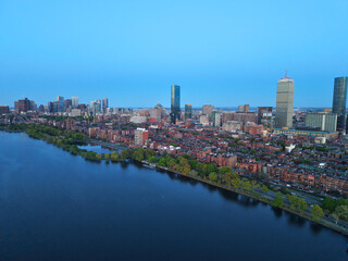 Obraz premium Golden hour aerial drone view of the Boston skyline, featuring the Prudential and John Hancock towers rising above the historic Back Bay neighborhood and the calm waters of the Charles River