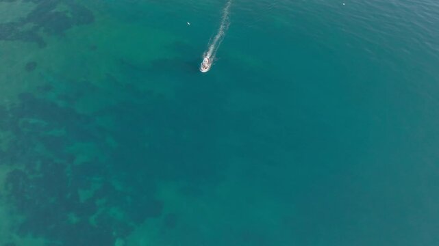 Aerial view of a small boat cruising through the turquoise waters near the Island of Ortigia with visible seabed patterns in Syracuse, Sicily, Italy.