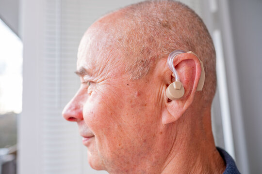 senior man with hearing aid, age-related hearing loss examining modern behind-the-ear, bte device hearing support, accessibility modern technology, inclusion, health care, confidence and everyday life